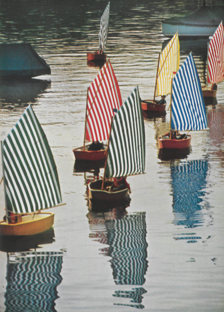 Bunte gestreifte Segelboote treiben auf ruhigem Wasser, das ihre Reflexionen zeigt.