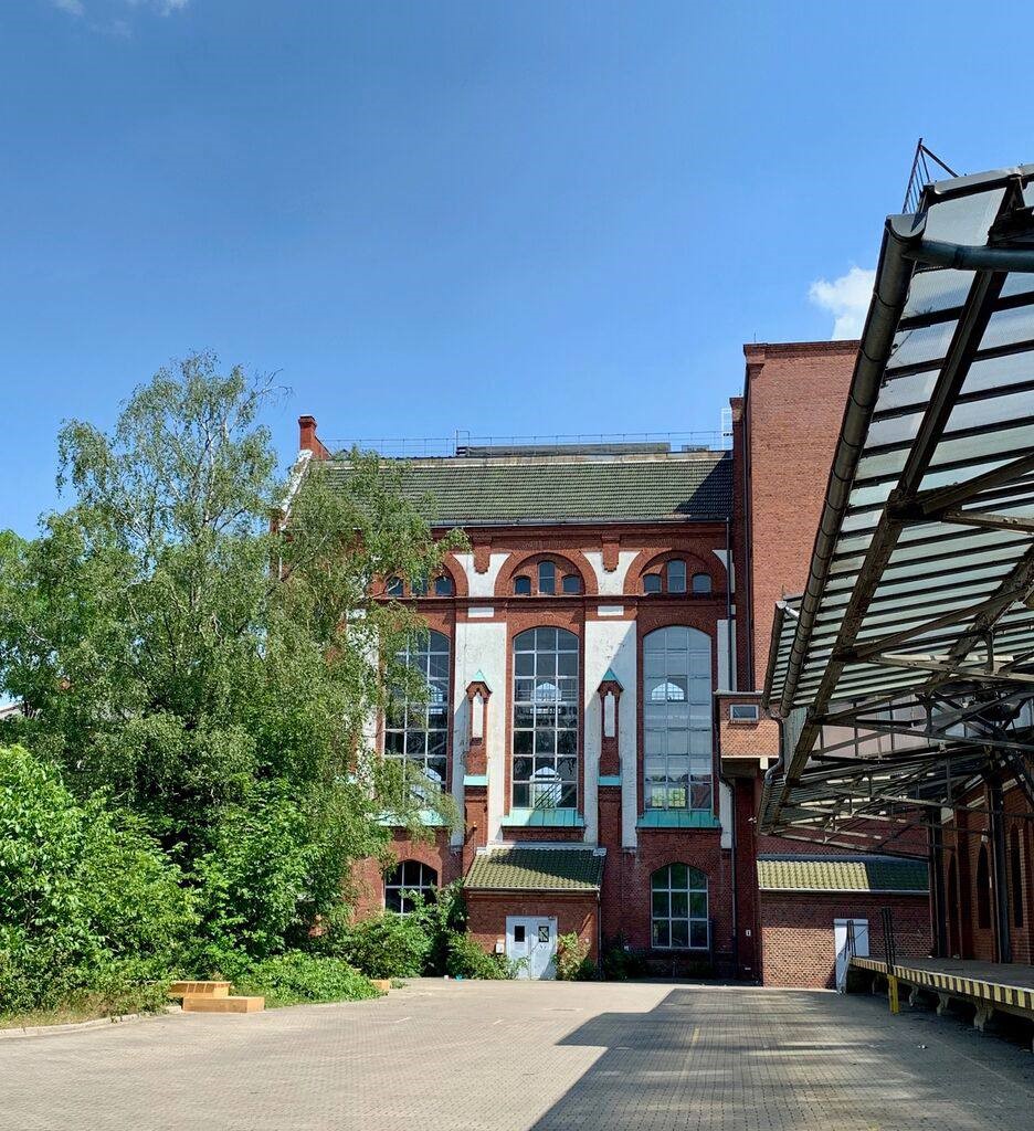 Historic building with large windows, surrounded by greenery and a blue sky.