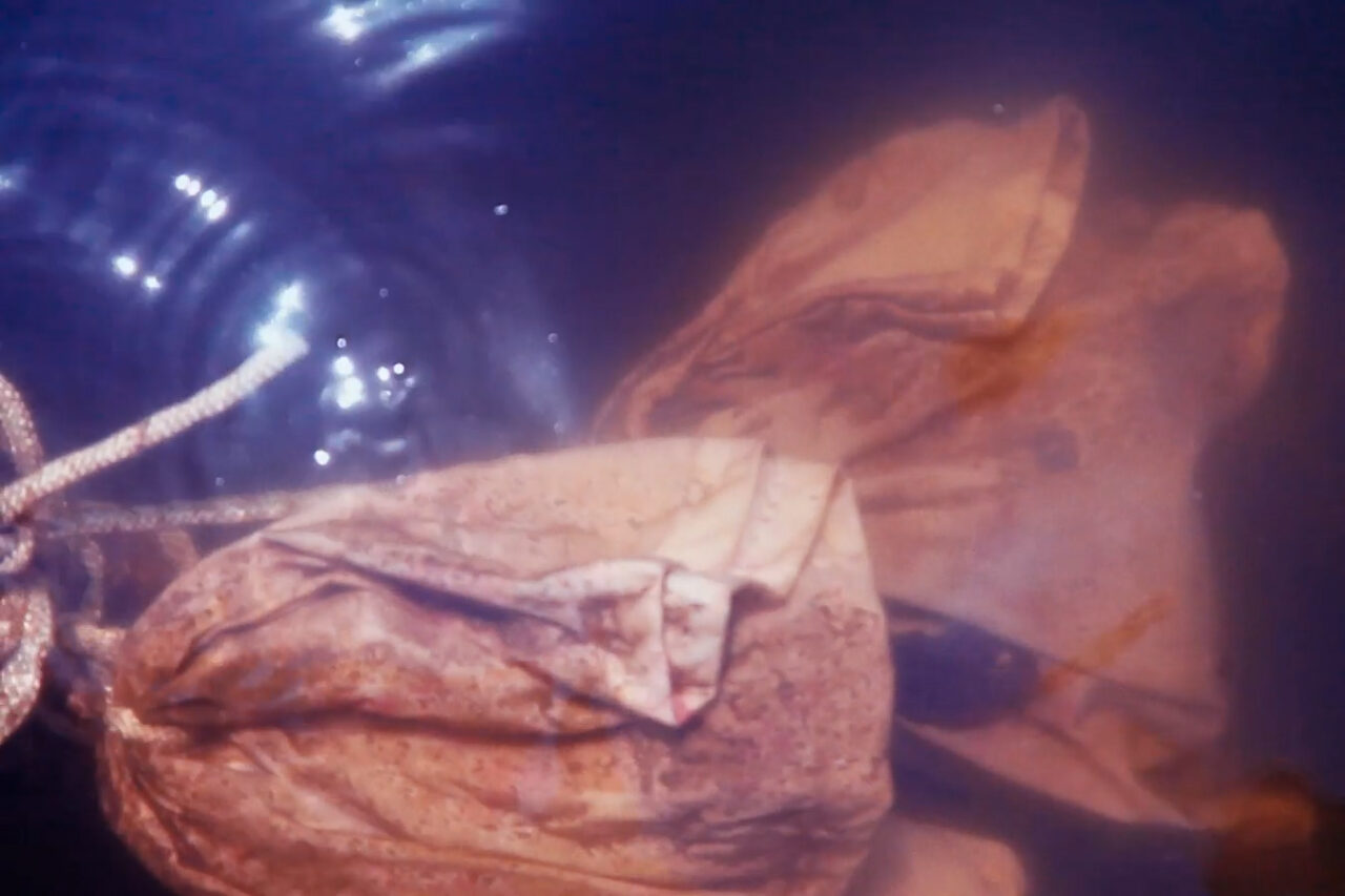 Material underwater, folded and weathered, partly in brown tones with wave-like patterns.