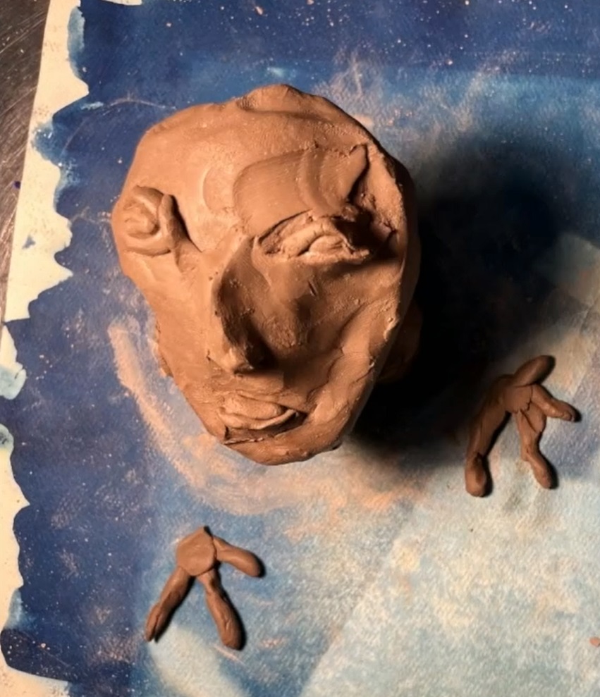 Tonfigur eines Gesichts mit zwei kleinen Tonfiguren vor einem blauen Hintergrund.