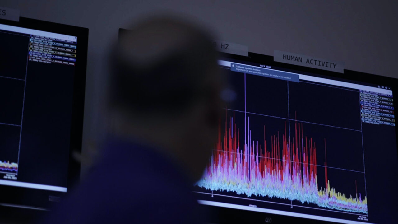 Person vor Monitoren mit bunten Spektraldiagrammen zur Datenvisualisierung.