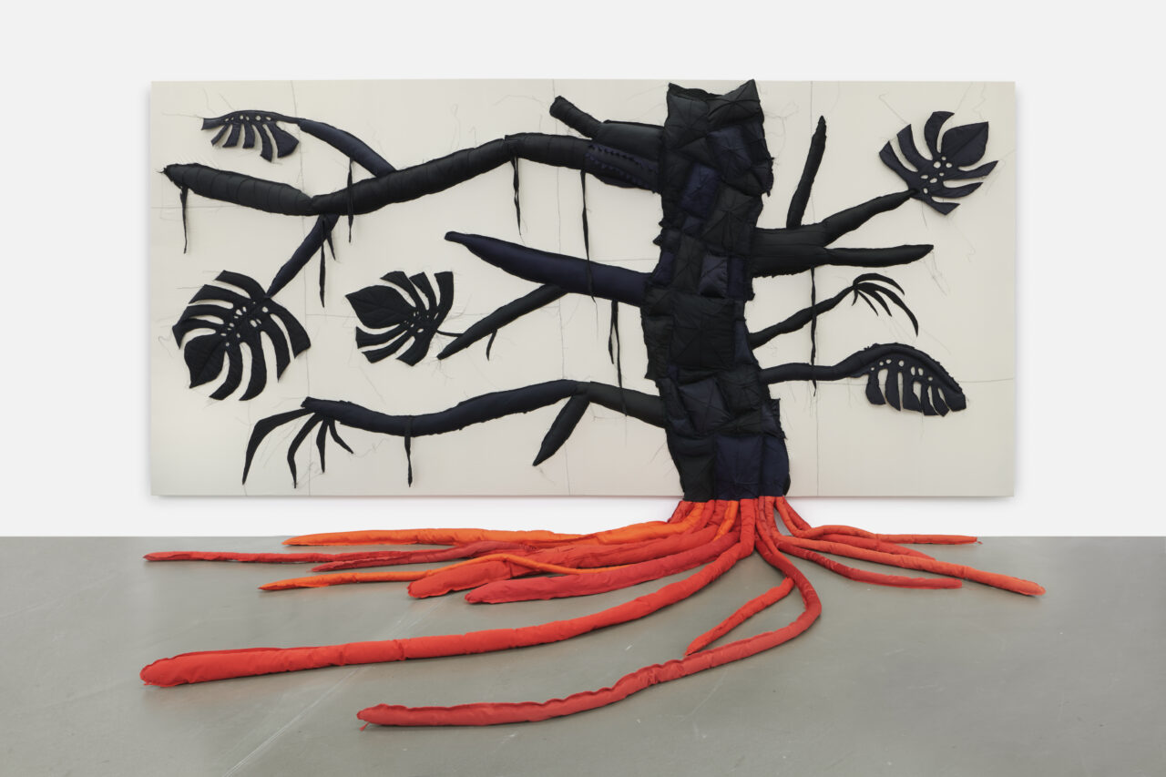 Art installation of a stylized tree with a black trunk and red roots, decorated with leaf motifs.