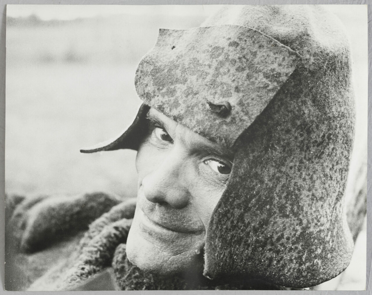 Portrait of a smiling soldier in a historical helmet, against a simple background.