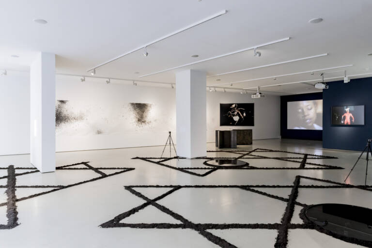 Moderne Kunstgalerie mit abstrakten Kunstwerken, Videoinstallationen und einem auffälligen, geometrischen Bodenlayout.