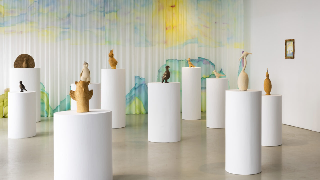 Skulpturen auf weißen Säulen in einem hellen, bunten Ausstellungsraum.