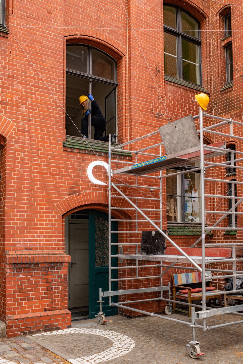 Workers on scaffolding next to a window of a red brick wall, wearing safety helmets.