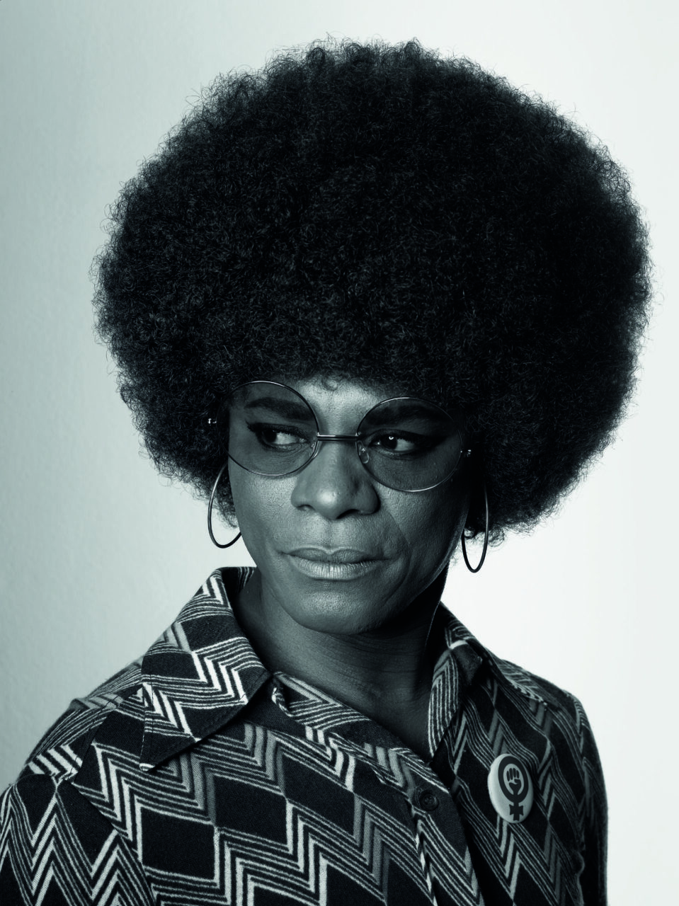 Portrait of a person with full Afro hair, sunglasses, and a black-and-white patterned shirt.