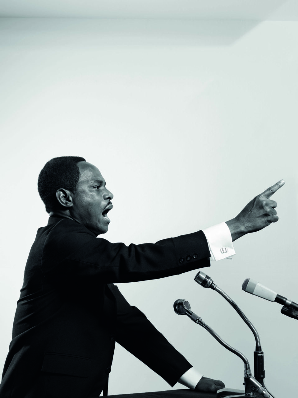 Man in a suit passionately speaks into a microphone and gestures with his hand.