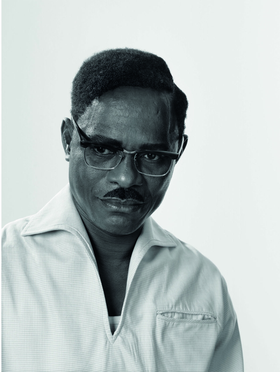 Black-and-white portrait of a man with glasses, a steady gaze, styled hair, smiling in a light shirt.