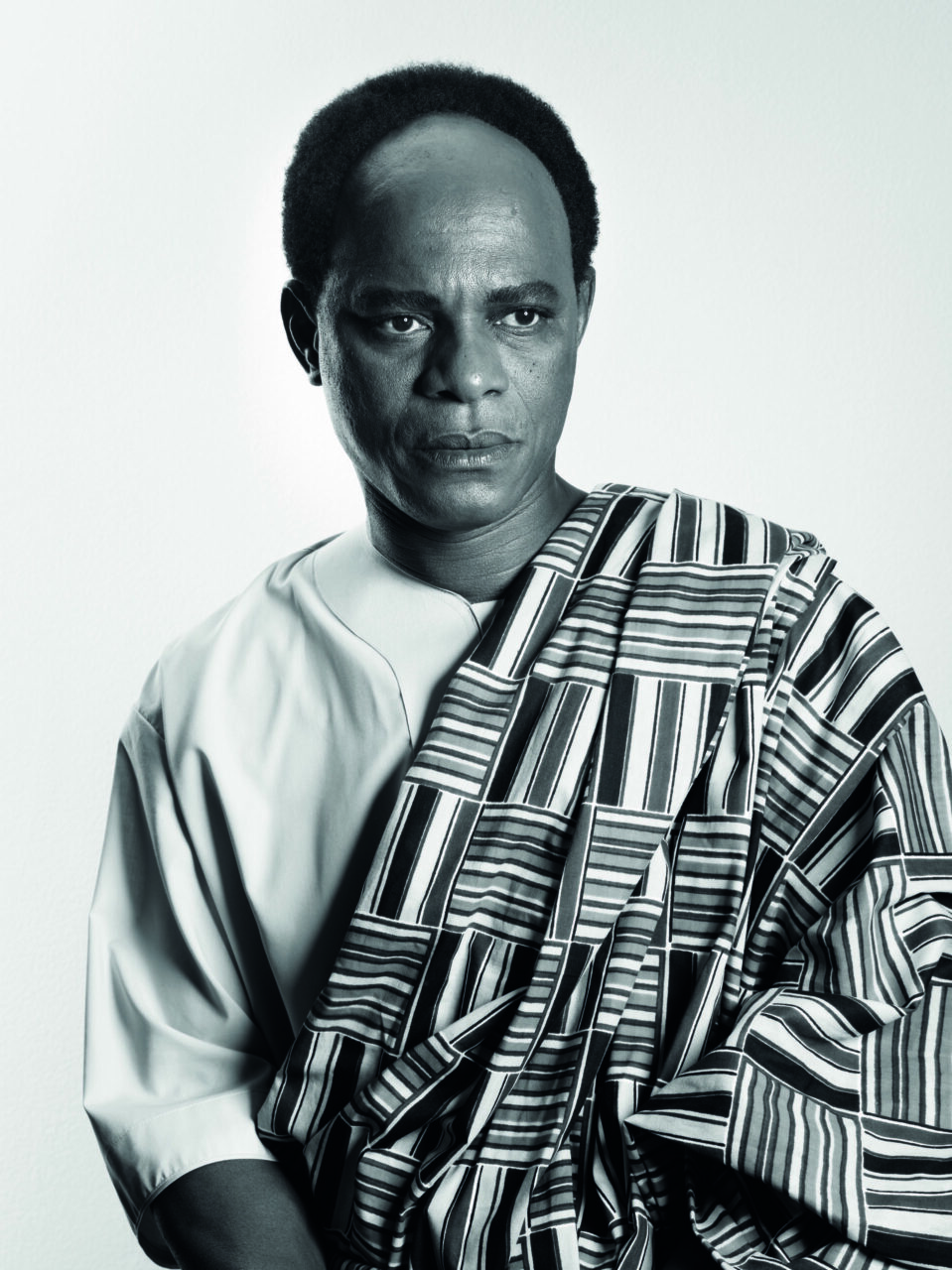 Portrait of a man in traditional clothing with a striped scarf, in black and white. His expression is serious and thoughtful.