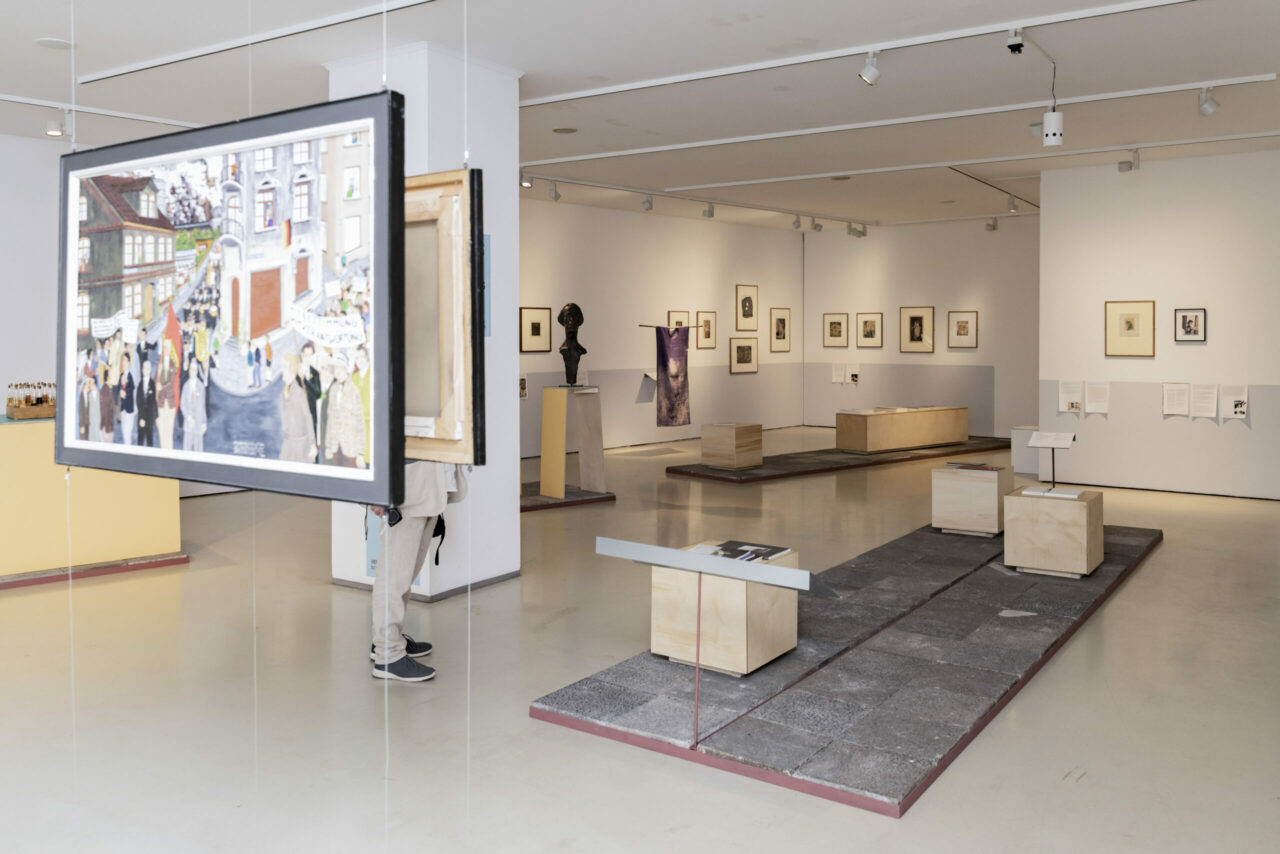 A view of a gallery with displayed artworks, including a large painting and sculptures.