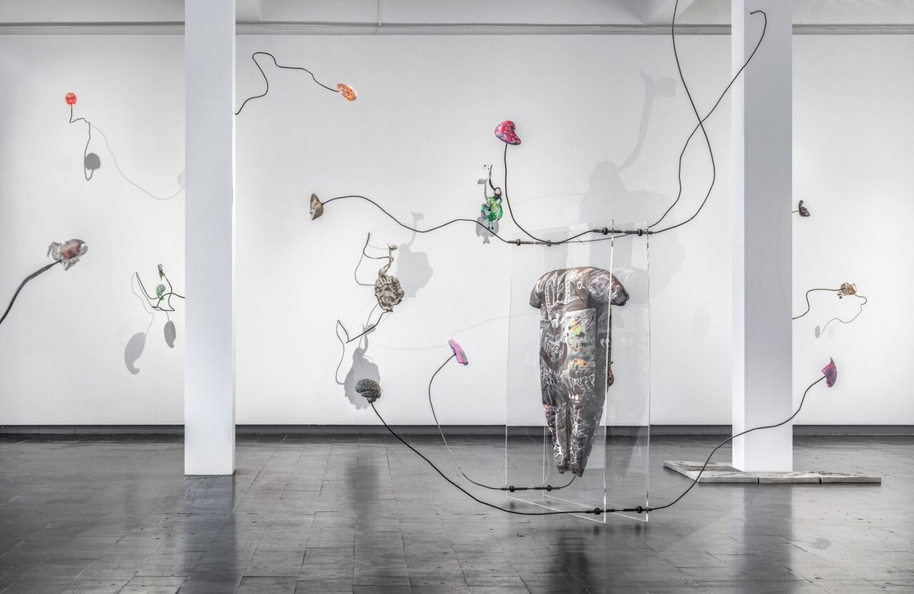 Modern art installation featuring a sculptural object and colorful needle cables on the wall.