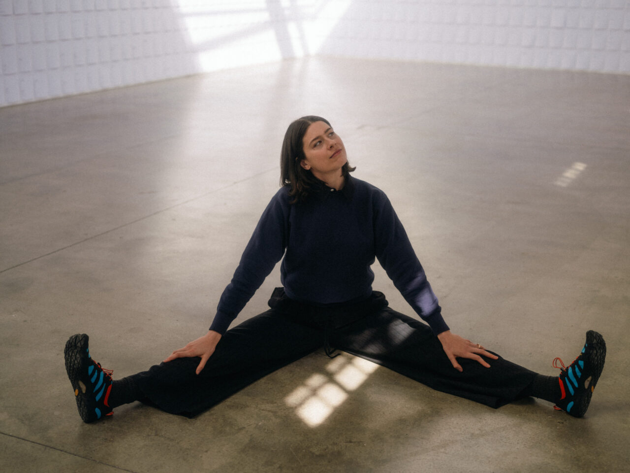 Junge Frau sitzt mit gespreizten Beinen auf dem Boden in einem modernen Raum.