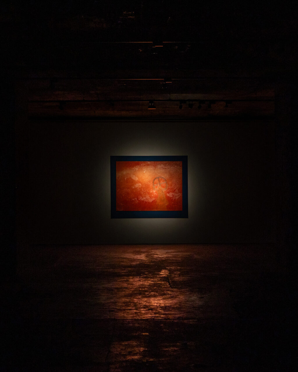 Dark room with a lit orange painting in a rectangular frame on the wall.