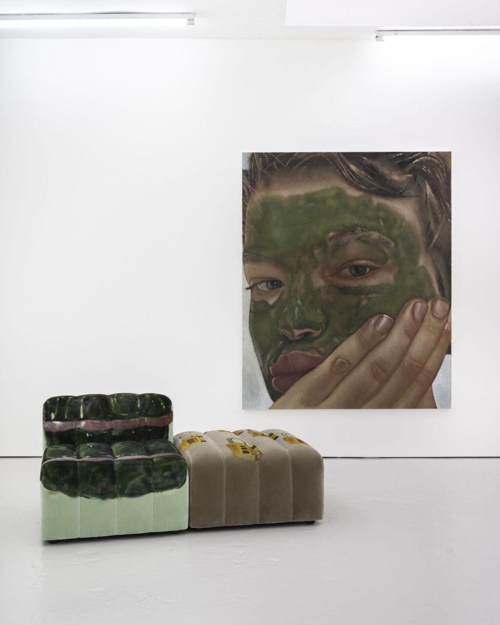 Kunstinstallation mit einem Gesichtsgemälde und zwei modernen Sitzmöbeln in einem weißen Raum.