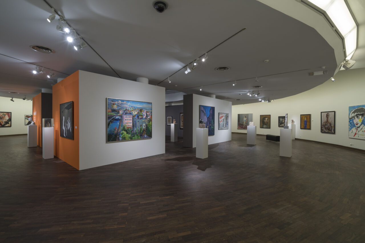 Modern art gallery with several exhibited paintings and sculptures, illuminated by ceiling spotlights.
