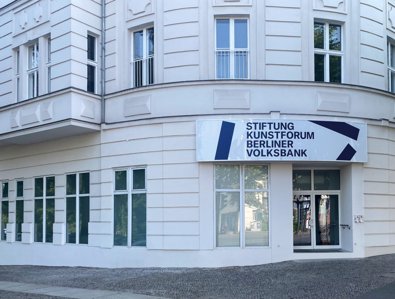 Entrance of the Kunstforum Berliner Volksbank on a bright day, featuring a large window front and an informational sign.
