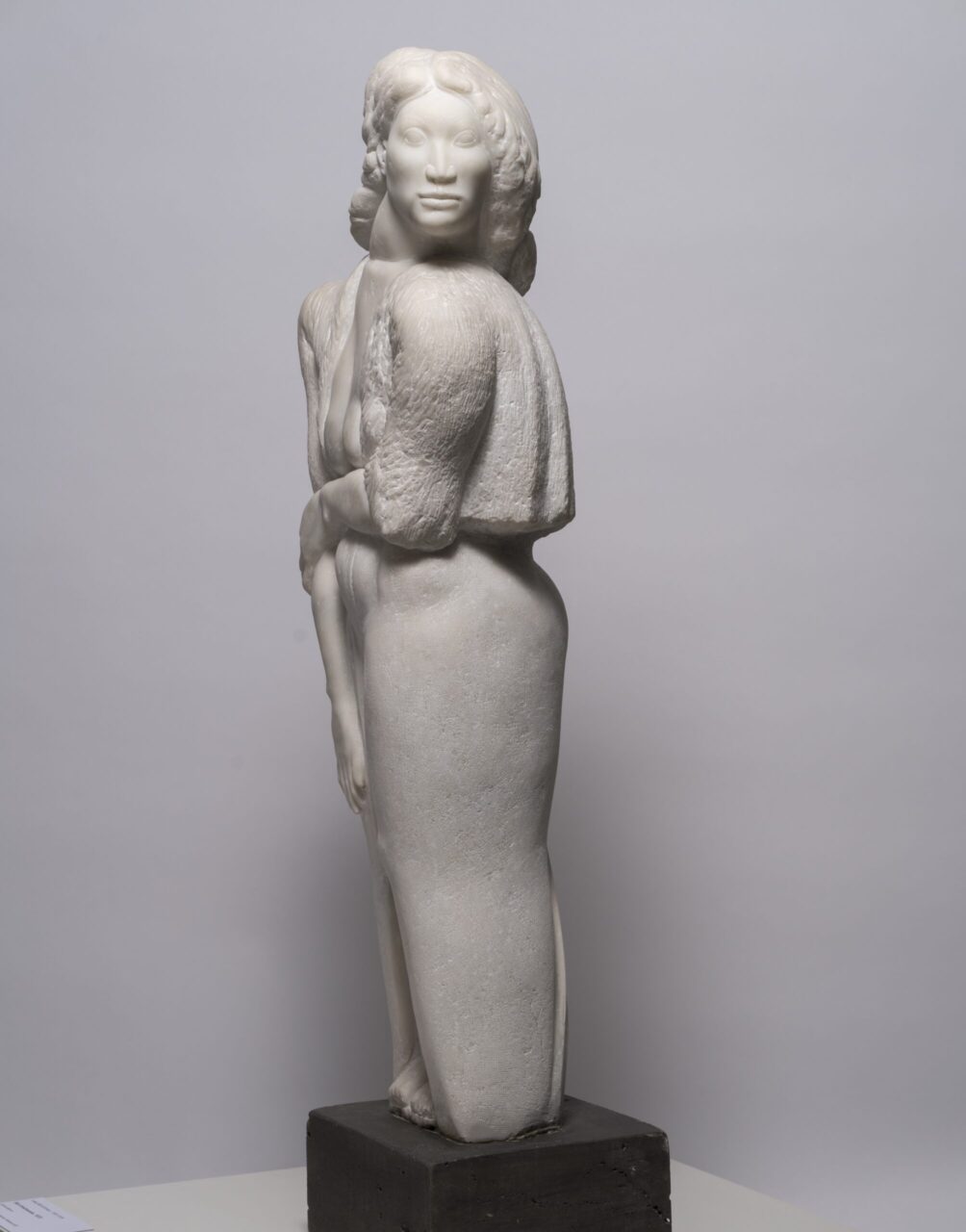 Sculpture of an elegant figure with embracing human sculptures, made of light material on a black pedestal.