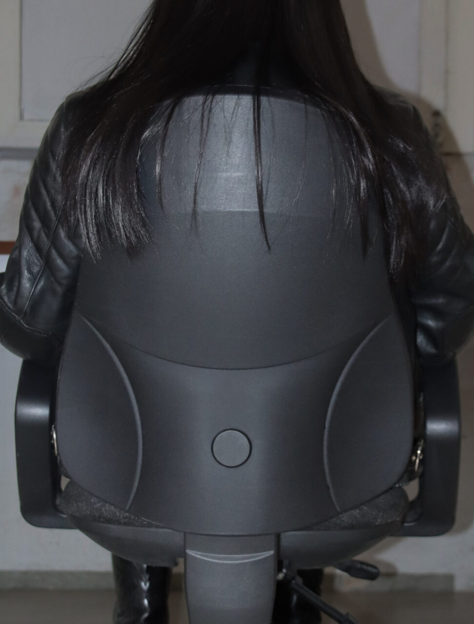 Eine schwarze B&uuml;rostuhlr&uuml;ckseite mit langen, glatten Haaren, die &uuml;ber die Lehne h&auml;ngen.