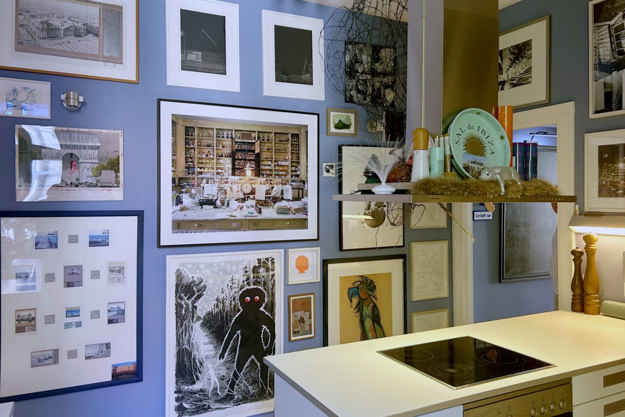Gallery wall with various framed artworks above a modern kitchen counter and stovetop, set against a blue backdrop.