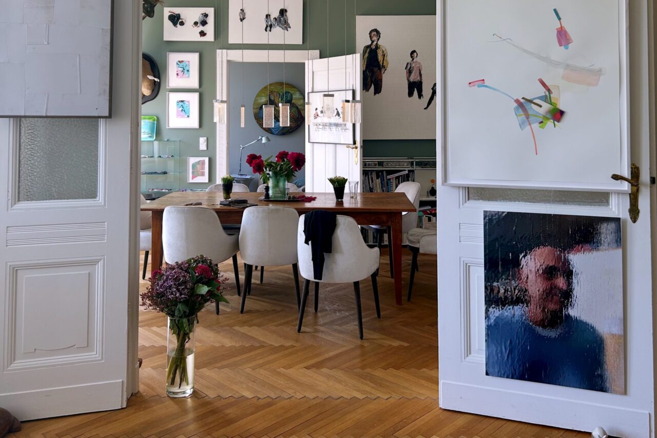 Stilvolles Interieur mit Esstisch, wei&szlig;en St&uuml;hlen, Kunstwerken an den W&auml;nden und Blumen in einer Vase f&uuml;r eine gem&uuml;tliche Atmosph&auml;re.