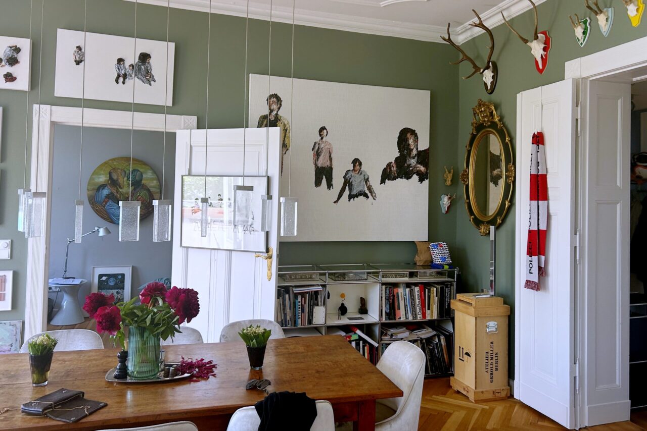 Ein gem&uuml;tliches Wohnzimmer mit gr&uuml;nen W&auml;nden, Kunstwerken, einem Holztisch und verschiedenen Dekorationen.