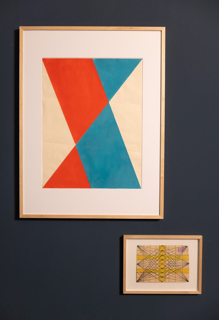 Geometric art pieces in frames, featuring red, blue, and yellow shapes on a dark wall.