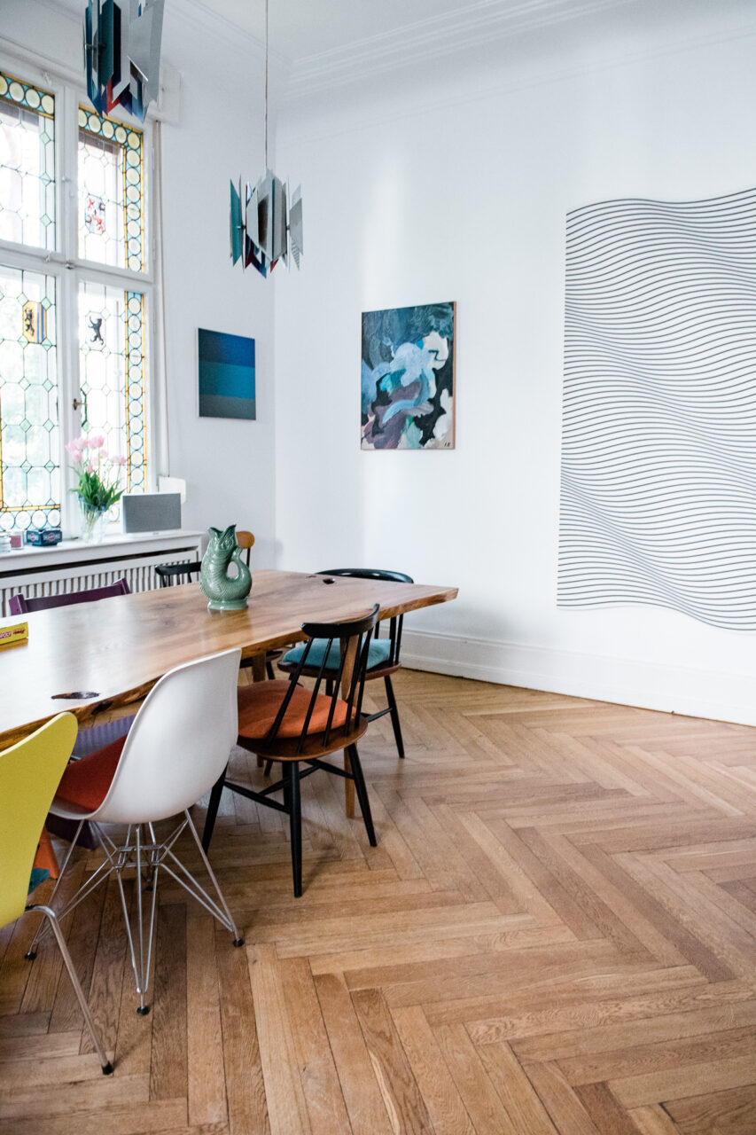 Modern dining area with a wooden tray, colorful chairs, and artwork on the wall. Bright, inviting atmosphere.