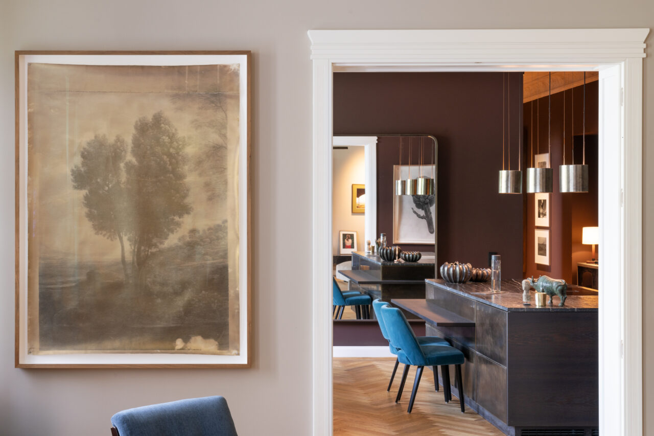 A room with an artistic painting, elegant decor, and modern lighting, visible through a door.