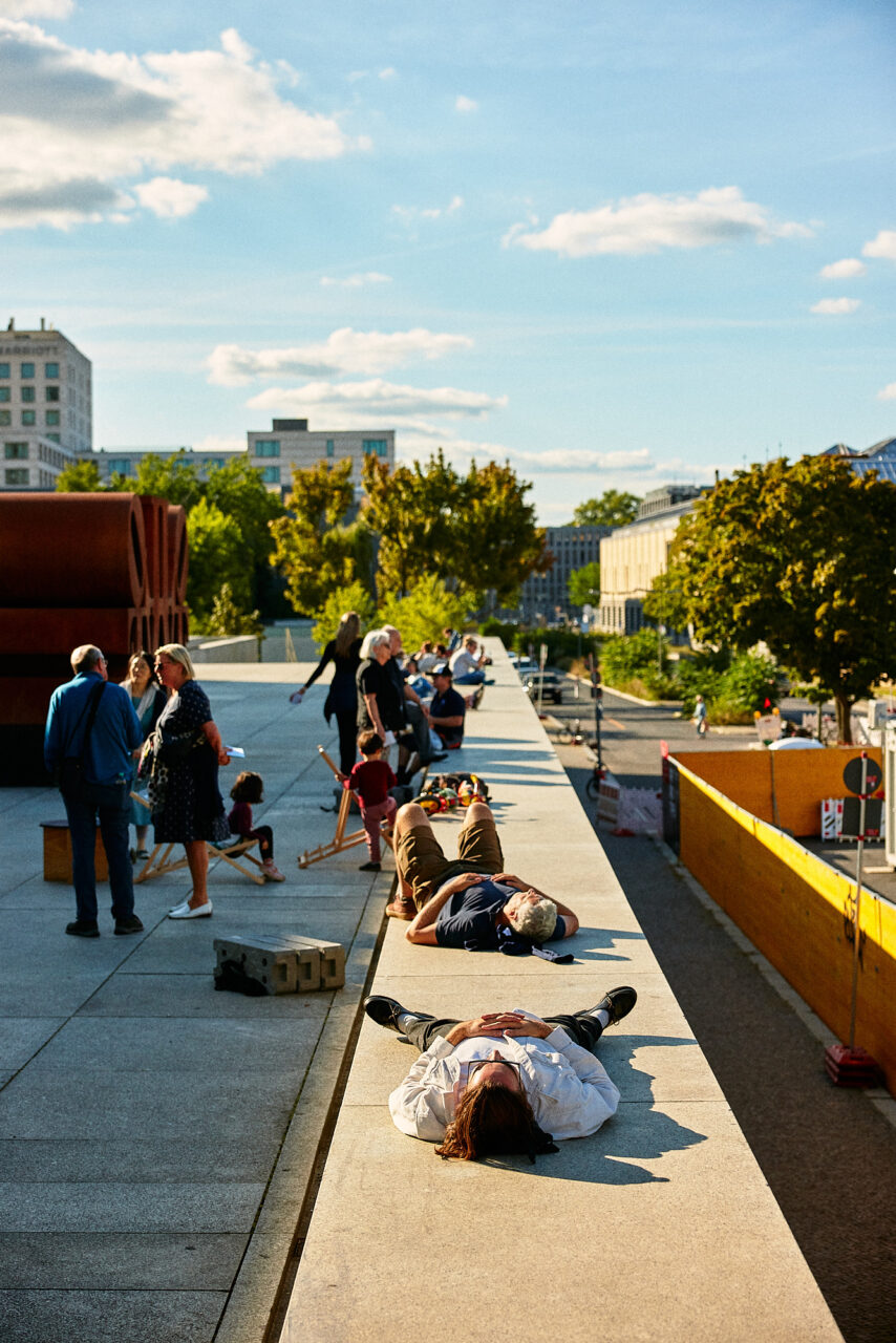 Menschen entspannen und unterhalten sich auf einer Mauer, w&auml;hrend andere darauf liegen, bei sch&ouml;nem Wetter.