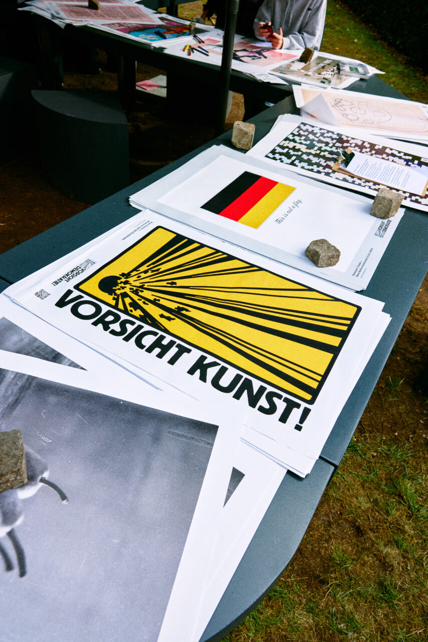 Eine &Uuml;bersicht von k&uuml;nstlerischen Postern und Druckmaterialien auf einem Tisch im Freien.